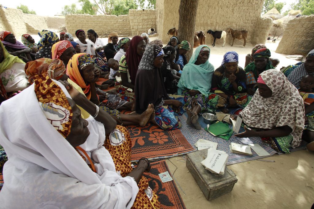 Large group of Nigerien women participating in a traditional VSLA system, sitting on carpets around a money box